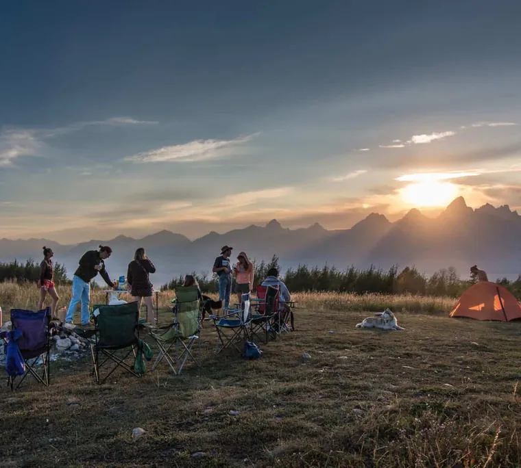 Campers gathered in a meadow at sunset below the Tetons